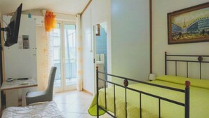 Quarto com cama, escrivaninha, cadeira, televisão e um quadro na parede.