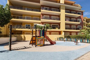 Ein mehrstöckiges Gebäude mit Balkonen, einem Spielplatz mit Rutsche und einem Poolbereich.