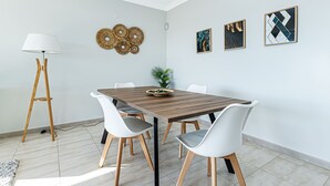 Uma sala de jantar com uma mesa de madeira, cadeiras brancas, um abajur e obras de arte nas paredes.