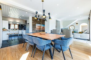 Eine moderne Küche mit Steinrückwand, ein Essbereich mit blauen Stühlen und ein Wohnzimmer mit grauem Sofa.