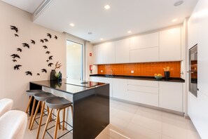 Een moderne keuken met een centraal eiland, barkrukken, witte kasten en een decoratief kunstwerk van vogels.