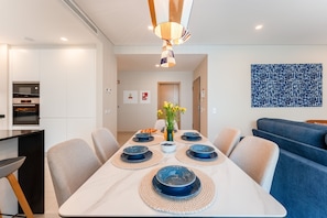 Een moderne eethoek met een witte tafel, blauwe borden en een decoratieve vaas.