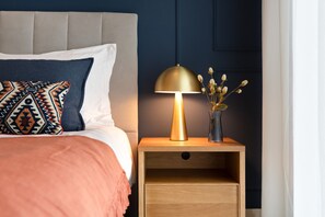 Een opgemaakt bed met gestreepte kussens, een bedlampje en een nachtkastje met een bloevas.