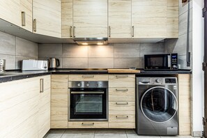 A modern kitchen with wooden cabinets, a built-in oven, a microwave, and a washing machine. - Cozy Place Lagos Apartment | Beach | Couples & Nom (Lagos)