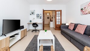 A modern living room with a TV, sofa, coffee table, and a desk with a chair. - Cozy Place Lagos Apartment | Beach | Couples & Nom (Lagos)