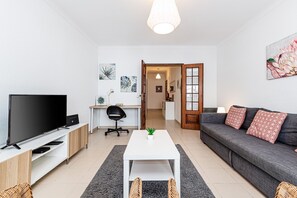 Ein modernes Wohnzimmer mit Fernseher, Sofa, Couchtisch und Schreibtisch mit Stuhl.