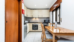 A compact kitchen with wooden cabinets, a built-in oven, a microwave, and a dining area with a wooden table and chairs. - Cozy Place Lagos Apartment | Beach | Couples & Nom (Lagos)