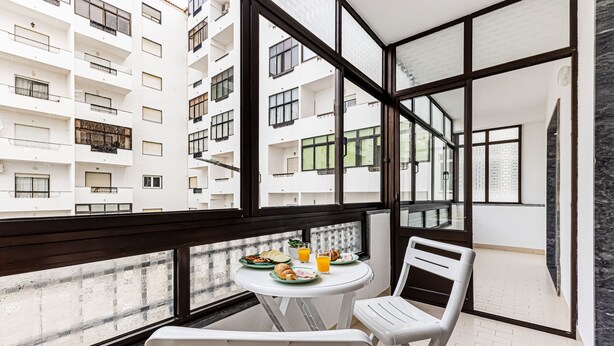 A balcony with a table set for breakfast, white chairs, and a view of adjacent buildings. - Cozy Place Lagos Apartment | Beach | Couples & Nom (Lagos)