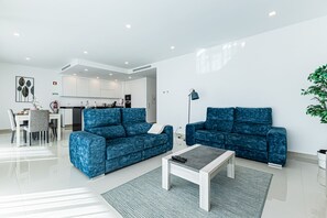 Ein modernes Wohnzimmer mit zwei blauen Sofas, einem Couchtisch und einem Essbereich mit Tisch und Stühlen.
