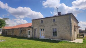 Ein zweistöckiges Steinhaus mit rotem Ziegeldach, einer kleinen Veranda und einem Schornstein.