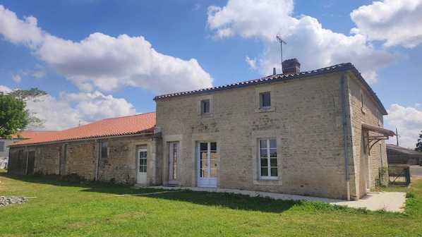 A two-story stone building with a red-tiled roof, a small porch, and a chimney.