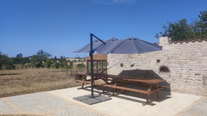 An outdoor seating area with a table and benches, a stone wall, and a clear blue sky. - Gîte de la Pointe: A Peaceful Country Retreat (Xanton-Chassenon)