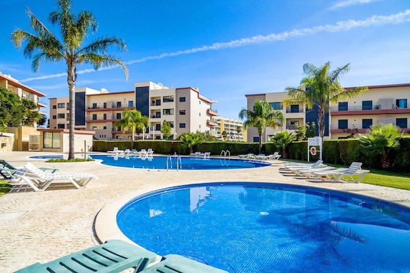 A swimming pool with lounge chairs, palm trees, and a building with multiple balconies. - Encosta By The Marina, Beach & City Center (Lagos)