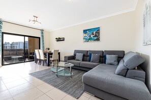 A modern living room with a grey sofa, a glass coffee table, and a dining area with chairs and a table. - Encosta By The Marina, Beach & City Center (Lagos)