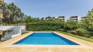 En rektangulär swimmingpool med en kant av kakel, omgiven av en vacker trädgård och en häck.