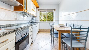 Ett modernt kök med en inbyggd ugn, ett matbord med stolar och ett fönster med utsikt över grönområden.
