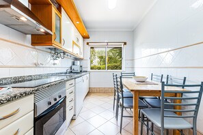 Eine moderne Küche mit Einbauofen, einem Esstisch mit Stühlen und einem Fenster mit Blick auf Grünflächen.