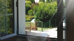 A view through a glass door to a building with a fenced yard and a white building with a red roof in the background. - A comfortable, air-conditioned bed-and-breakfast on the Grands Crus Route in Gilly (Gilly les Citeaux)