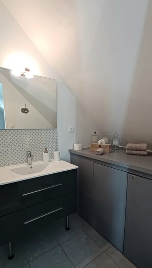 Een moderne badkamer met een witte wastafel, donkere kastjes en een betegelde spatwand.