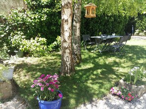Un jardín con un árbol, un comedero para pájaros y una mesa con sillas.