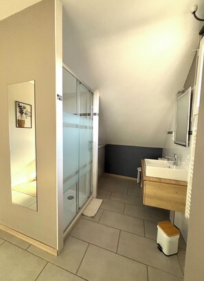 Un baño con cabina de ducha de vidrio, lavamanos con tocador de madera y espejo sobre el lavamanos.