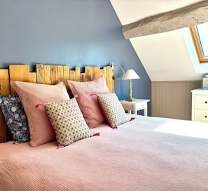Ein Schlafzimmer mit schrägem Dach, einem Holzkopfende, einer Nachttischlampe und einem blumigen Kissen.