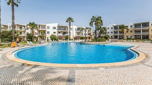 Ein Pool, umgeben von einer gepflasterten Fläche mit Liegestühlen und Palmen.