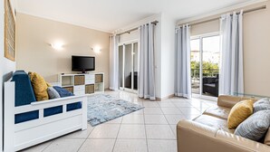 Ein modernes Wohnzimmer mit einer Couch, einem Fernseher und einer Glastür zum Balkon.