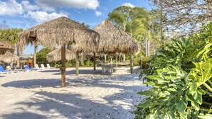 A beach with thatched umbrellas, lounge chairs, and a sandy area with a palm tree. - 2nd Floor Condo w/ Basketball Court, Restaurant, Balcony, Gym, Near Theme Parks (Davenport)