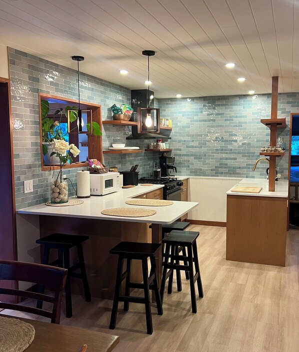 A modern kitchen with a central island, bar stools, a built-in oven, and a backsplash with blue tiles.