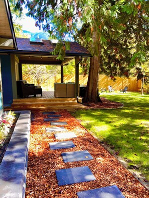 A covered patio area with outdoor furniture, a stone pathway, and a lawn.