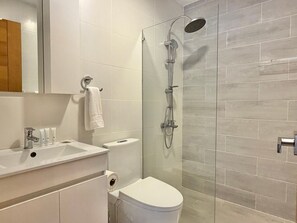 Moderni kylpyhuone, jossa on lasiseinällä varustettu suihku, valkoinen pesuallas ja wc.