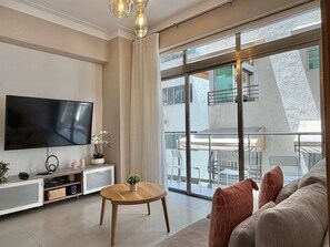 Ein modernes Wohnzimmer mit Flachbildfernseher, einem runden Holztisch, einer Couch und einem Balkon mit Gartenmöbeln.