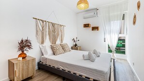 A modern bedroom with a bed, bedside tables, a hanging macrame wall decoration, a pendant light, and an air conditioning unit. - Casa Sol | Vilamoura (Vilamoura)