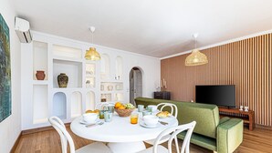 A dining area with a round table, white chairs, and a green sofa. - Casa Sol | Vilamoura (Vilamoura)