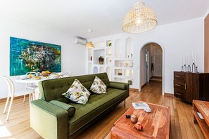 A modern living room with a green sofa, wooden coffee table, and a dining area with white chairs. - Casa Sol | Vilamoura (Vilamoura)