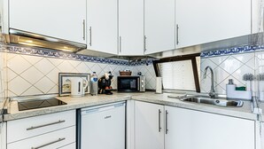 Una cocina con armarios blancos, lavavajillas integrado, microondas y un fregadero.
