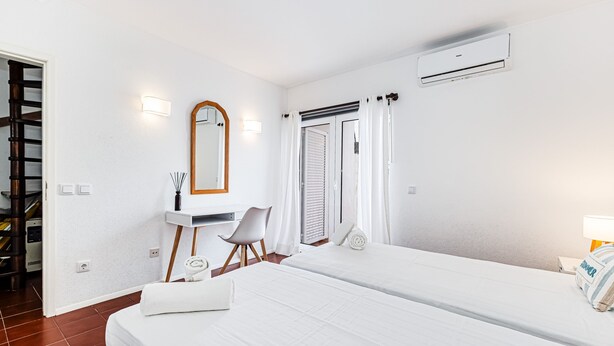 Una habitación de hotel con cama, escritorio, silla, espejo y equipo de aire acondicionado.