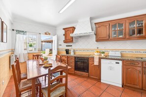 Eine Küche mit Holzausstattung, einem Esstisch mit Stühlen, einem eingebauten Backofen und einem Geschirrspüler.