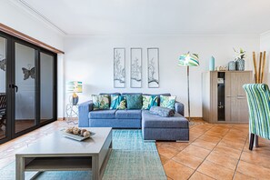Un salon avec un canapé bleu, une table basse, un tapis à motifs et des œuvres d’art murales.