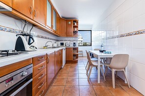 A kitchen with wooden cabinets, a microwave, a kettle, and a dining area with a table and chairs. - Sea La Vie | On the Beach, City Center & Marina (Lagos)