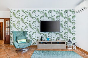 A living room with a teal armchair, a flat-screen TV, a wooden TV stand, and a patterned wall. - Sea La Vie | On the Beach, City Center & Marina (Lagos)