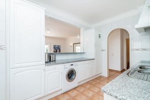 Een moderne keuken met witte kasten, een ingebouwde wasmachine, granieten werkbladen en een betegelde spatwand.
