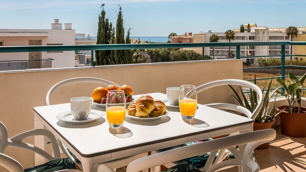 Ein Balkon mit einem Frühstückstisch, gedeckt mit Croissants, Obst und Orangensaft.