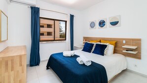 Une chambre à coucher comprenant un lit, une table de chevet, une fenêtre avec des rideaux et des œuvres d’art murales.