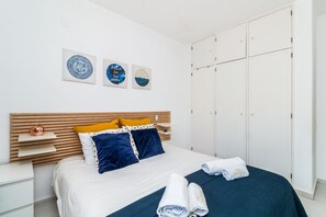 Ein Schlafzimmer mit Bett, Kissen, Kopfteil, Nachttisch, Kleiderschrank und Wandbildern.