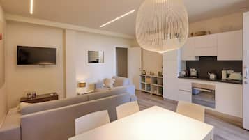 Una sala de estar moderna con sofá, mesa de comedor y zona de cocina con armarios y hervidor.