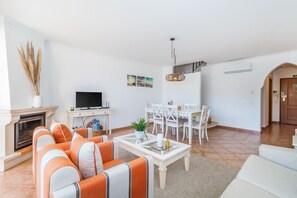 Een woonkamer met een open haard, bank, eettafel en stoelen.