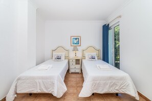 Een kamer met twee bedden, een nachtkastje, een ingelijst plaatje en een raam met gordijnen.