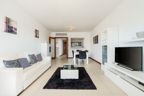 Ein modernes Wohnzimmer mit einem weißen Sofa, einem schwarzen Teppich, einem Fernseher und einem Essbereich.
